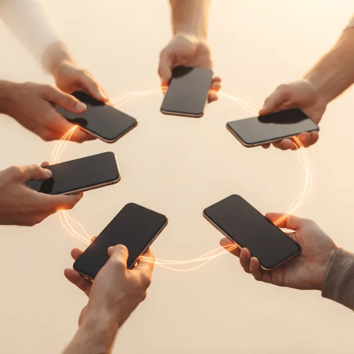Várias mãos segurando celulares em roda, ligadas por um fio de luz